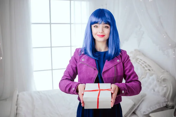 Mode-Freak. Porträt von Glamour lächelnde schöne Frau mit blauen Haaren hält Geschenk im weißen Schlafzimmer. Mode- und Schönheitskonzept — Stockfoto