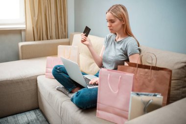 Evde alışveriş online. Kredi kartı olan ciddi kadın büyük satış online alışveriş alışveriş torbaları ile bir kanepede otururken arıyor