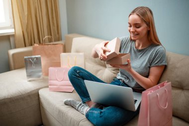 Evde alışveriş online. Alışverişçi gülümseyen genç onun parsel unboxing ve bakarak, sipariş edilen ve Internet tarafından teslim edildi