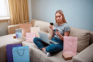 Evde alışveriş online. Dizüstü bilgisayar ile genç mutlu müşteri online mağazasında alışveriş torbaları ile bir kanepede otururken en iyi kredi kartı ödeme için seçmektir