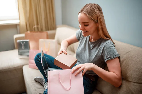 Compras en línea en casa. Joven mujer emocionada es unboxing su paquete, ordenado por Internet, mientras está sentado en el sofá — Foto de Stock