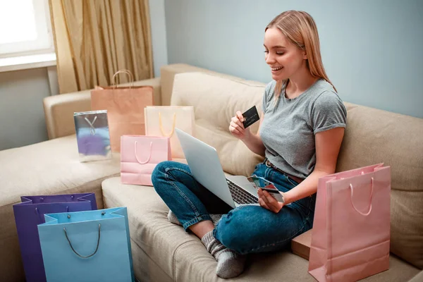Compras en línea en casa. Joven comprador feliz con tarjetas de crédito está eligiendo la mejor venta de viernes negro mientras está sentado en un sofá con bolsas de compras — Foto de Stock