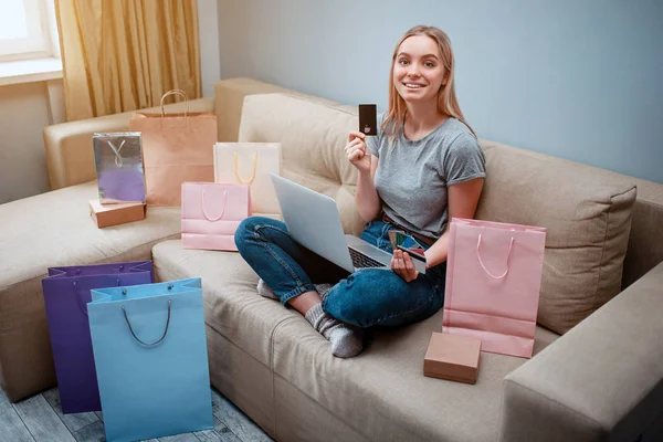Compras en línea en casa. Joven comprador feliz con tarjetas de crédito está eligiendo la mejor venta del día de solteros mientras está sentado en un sofá con bolsas de compras — Foto de Stock