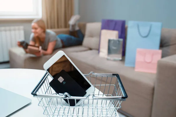 Compras en línea en casa. Tarjeta de crédito y teléfono inteligente en el fondo de una mujer con bolsas de compras — Foto de Stock