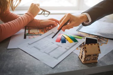 Çift satın almak ya da Kiralık Daire birlikte. Erkek ve kadın el görünümünü kesti. Dokuların renkli parçalar tutun. O kalemle daire planı gelin. Tablo küçük ahşap oyuncak ev.