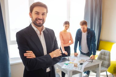 Çift satın almak ya da Kiralık Daire birlikte. Pozitif profesyonel görünüm ve poz fotoğraf makinesinde. O gülümseme. İki tablo standında arkasında. Daire planları görünüyorlar.