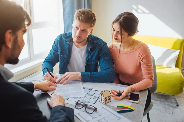 Pareja comprar o alquilar apartamento juntos. Trato de negocios. El joven puso la firma en los documentos y mira a los agentes inmobiliarios. Señala el documento . — Foto de Stock