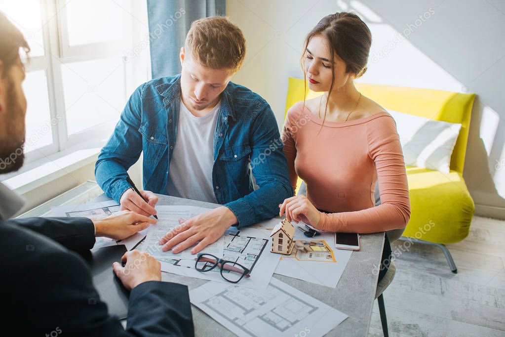 Couple buy or rent apartment together. Serious concentrated man put signature on documents. Business deal. Young woman look at it. Realtor sit in front of them.