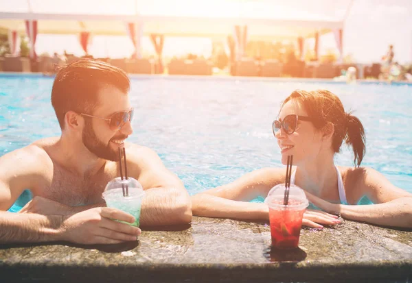 Pareja joven junto a la piscina. Hombre y mujeres bebiendo cócteles en el agua . — Foto de Stock