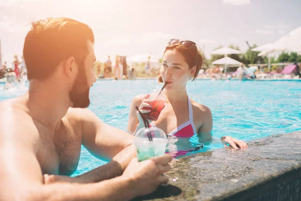 Pareja joven junto a la piscina. Hombre y mujeres bebiendo cócteles en el agua . — Foto de Stock