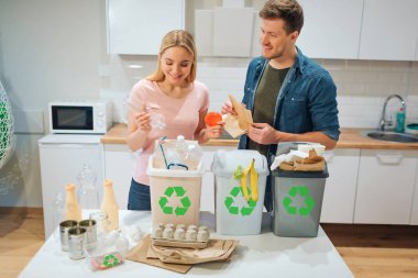 Evde atık sıralama. Mutfak plastik, kağıt, çöp biyo kutuları diğer atık koyarak gülümseyen genç çift