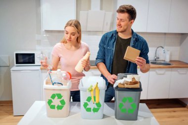 Evde atık sıralama. Mutfak plastik, kağıt, çöp biyo kutuları diğer atık koyarak gülümseyen genç Aile