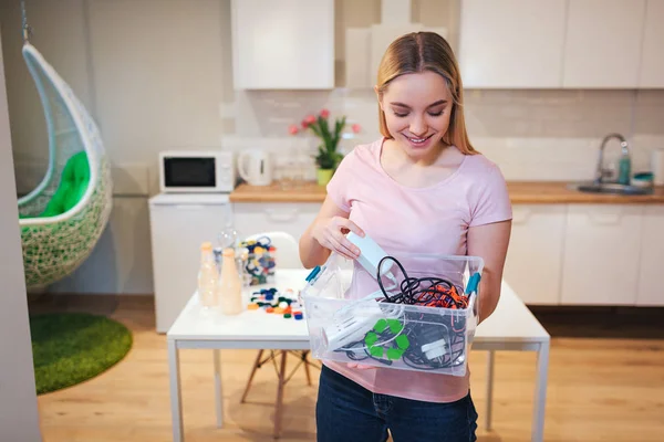 Geri dönüşüm. Genç gülümseyen kadın mutfak arka plan üzerinde yeşil geri dönüşüm simgesi ile konteyner elektronik atık tutarak — Stok fotoğraf