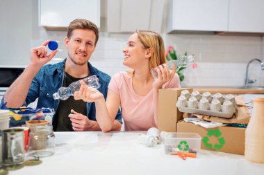 Geri dönüşüm. Evde diğer atık ile masada otururken farkında genç aile boş plastik şişe ve kapaklar sıralama