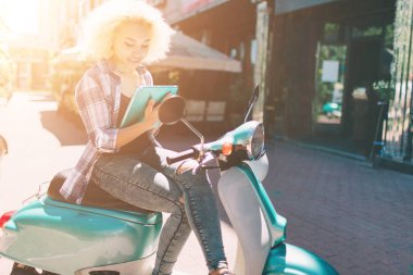 Neşeli genç kadın scooter üzerinde oturan ve dijital tablet kullanma.