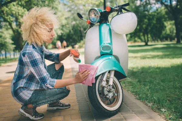 Afrikalı-Amerikalı kadın motorlu scooter yıkama. Temizlik kız bir mavi moped veya motosiklet. — Stok fotoğraf