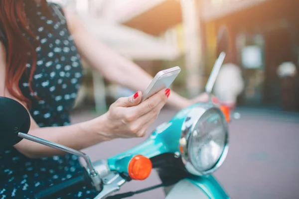 Gyönyörű fiatal nő öltözve, alkalmi ül a scooter és a telefon Holdind. Lány ül a kerékpáros és használata mobiltelefon okostelefon — Stock Fotó