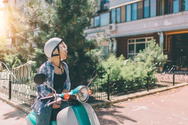 Молодая веселая девушка водит скутер в городе. Портрет молодой и стильной женщины с мопедом — стоковое фото