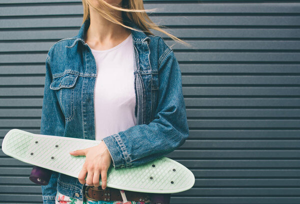 Young blonde woman with a skateboard in his hand against the background of a Striped wall