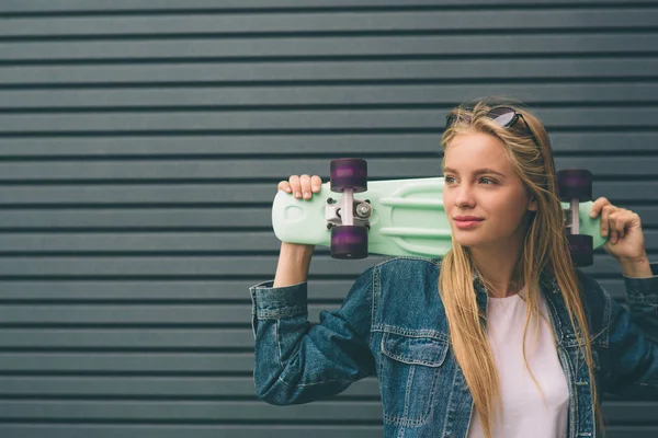 Молодая блондинка со скейтбордом в руке на фоне полосатой стены — стоковое фото