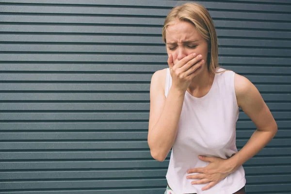 Genç kadın elle mide gri arka plan üzerinde izole kötü ağrı acı çekiyor. Gıda zehirlenmesi, grip, krampları. Sağlık sorunları sorunları kavramı.