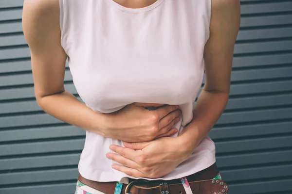 Genç kadın elle mide gri arka plan üzerinde izole kötü ağrı acı çekiyor. Gıda zehirlenmesi, grip, krampları. Sağlık sorunları sorunları kavramı.