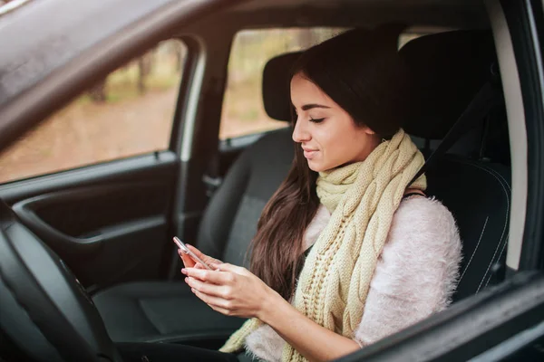 Belle femme souriant tout en étant assis dans la voiture. Fille utilise un smartphone . — Photo