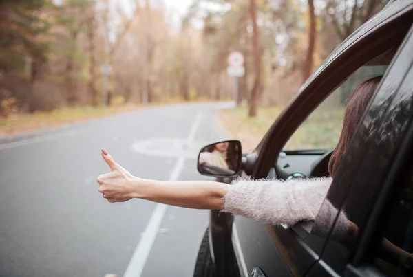 Viajera en la carretera sosteniendo los pulgares hacia arriba. Vacaciones de otoño, vacaciones, viajes, viajes por carretera y concepto de personas. Cierra la mano. Concepto de otoño. Viaje del bosque otoñal en coche — Foto de Stock