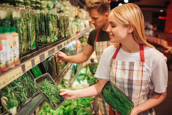 Jovem e mulher estão na prateleira da vegetação na mercearia. Puseram-no no seu lugar. Os trabalhadores sorriem. Feliz e positivo . — Fotografia de Stock