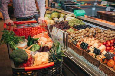 Bakkal dükkanında yalnız genç bir adam. Kesme görünümü adam arabası el tutun. Sebze ve meyve dolu sepet. İyi bakkal ile sepetler ayakta.