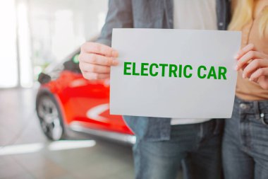Genç aile showroom ilk elektrikli araba satın. Yakın çekim el kağıdı ile kelime elektrikli araba tutarak. Çevre koruma için Eko pil elektrikli araba.