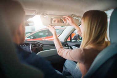 Genç aile showroom ilk elektrikli araba satın. Çekici kadın test sürüş önce modern elektrik hibrid aracın kabin ayna içine bakıyor. Elektrikli araba satış konsepti