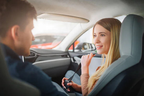 Jeune famille achetant la première voiture électrique dans le showroom. Couple souriant attrayant parlant dans la cabine d'un véhicule hybride électrique moderne avant de tester la conduite. Concept de vente de voiture électrique — Photo