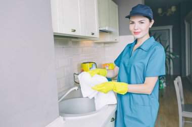 Güzel esmer lavabo standları ve beyaz havlu tutar. Güven ile kameraya bakıyor. Kız mavi kap ve üniforma giyer. Ayrıca o sarı eldiven vardır.