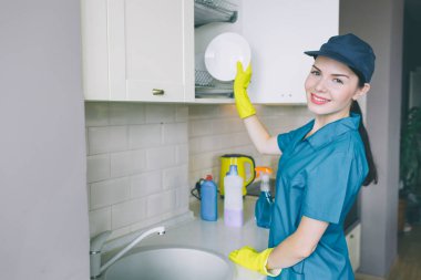 Lavabo ve göz fotoğraf makinesinde olumlu ve enerjik bir kız durur. O gülümsüyor. Kadın plaka dolaba koyar. Dikkatli bakıyor. Kız profesyonel temizleyicisidir.