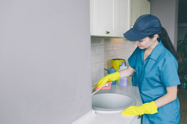 Lavabo ve tüp yıkama dikkatli kız stnds. O turuncu bez kullanır. Kız Tube bir el ve diğer bir tablo tutar.