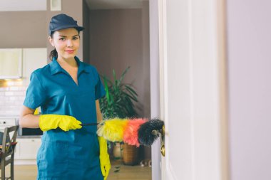 Esmer standları ve kameraya poz veriyor. O toz fırça tutar. Kız sarı eldivenler koruma ve mavi üniforma giyer.