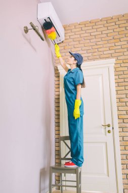 Kız portresi sandalye üzerinde duruyor ve örnek alıyor. O çalışıyor. Kız Klima Nick toz fırçası temizler. Tek eliyle çalışıyor.