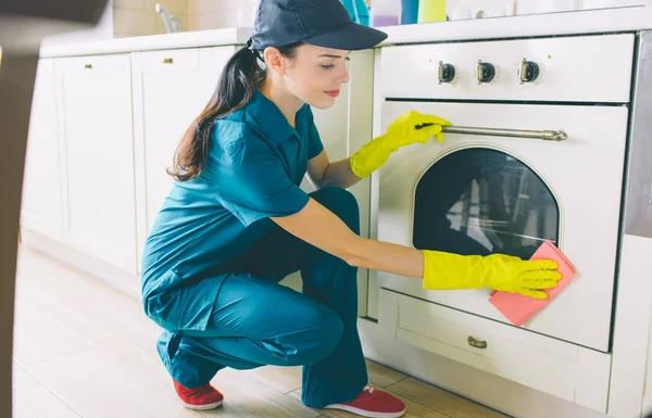 Una imagen de limpiador sentado en la posición de escuadrón y la estufa de lavado. Usa trapo naranja. La chica limpia muy bien. Ella es una trabajadora dura . —  Fotos de Stock