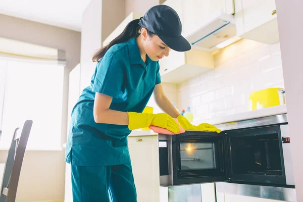 Cleaner stoi w kuchni i czyści powierzchni kuchenka owen. Ona robi to z rękawiczki i szmata. Dziewczyna jest spokojny i skoncentrowany. — Zdjęcie stockowe