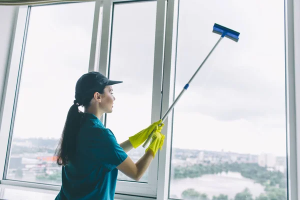 Een foto van schonere werken ter venster. Ze reinigt het met mop. Meisje is geconcentreerd. Ze doet voorzichtig. — Stockfoto