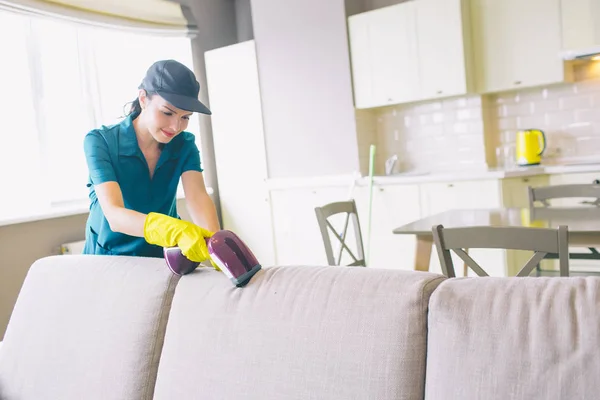 A picture of girl cleaning edge of sofa. She uses small vacuum cleaner. Woman is professional. She does work perfectly. — Stock Photo, Image