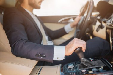 Arabada oturan ve sürüş sakallı genç adam görünümünü kesti. O direksiyon simidi üzerinde bir el ve el freni üzerinde başka bir tutar. Adam konsantre.