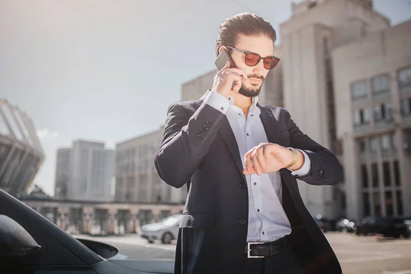 Un jeune homme sérieux et bien habillé marche dans la rue. Il parle au téléphone et regarde les montres. Il est pressé. Il tarde. . — Photo