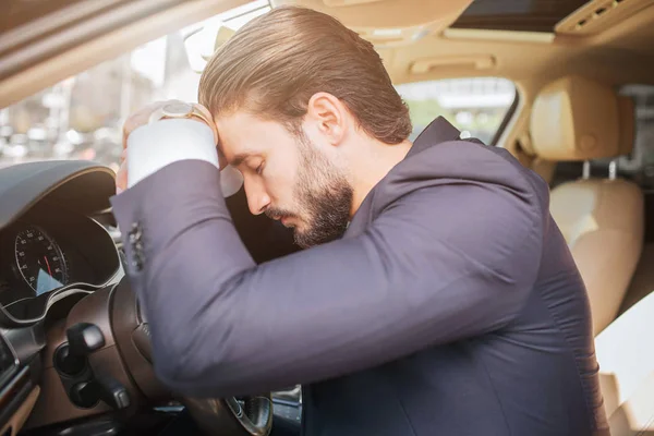 Уставший и измученный молодой бизнесмен садится на машину и прислоняется к рулю. Он держит глаза закрытыми. Молодой человек спит . — стоковое фото
