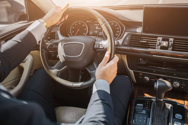 Вырезать вид человека руки в костюме. Парень сидит в машине и держит за руки руль. Он водит машину.
.