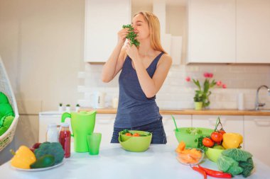 Vegan beautiful blonde woman enjoys the smell of organic parsley before cooking in kitchen. Vegetarian food. Healthy food. Vegan diet clipart