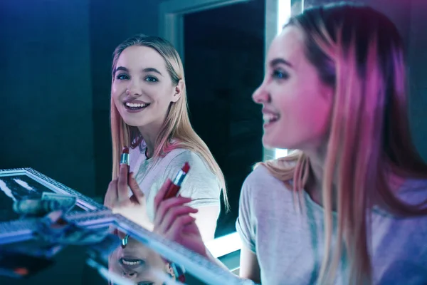 Drugs destroy you. Young drug addict laughs and paints her lips after taking drugs in night clubs toilet. Addicted woman near cocaine lines looks at the mirror. Drugs obsession