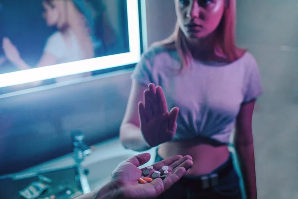 No drugs. Drug offer. Reject drugs offer. Hand saying NO. Young woman shows an open palm against drugs offer while hand holding drugs in night club. Stop drug addiction. 26 June, International Day