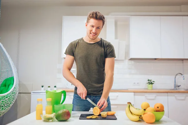 Mladý, usměvavý muž vaření čerstvého ovoce v kuchyni. Zdravé jídlo. Vegetariánské jídlo. Detoxikační dieta — Stock fotografie